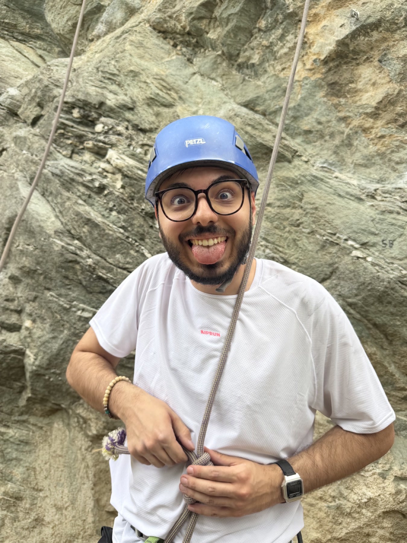 A climber in a blue helmet making a funny face while holding a rope at the crag.